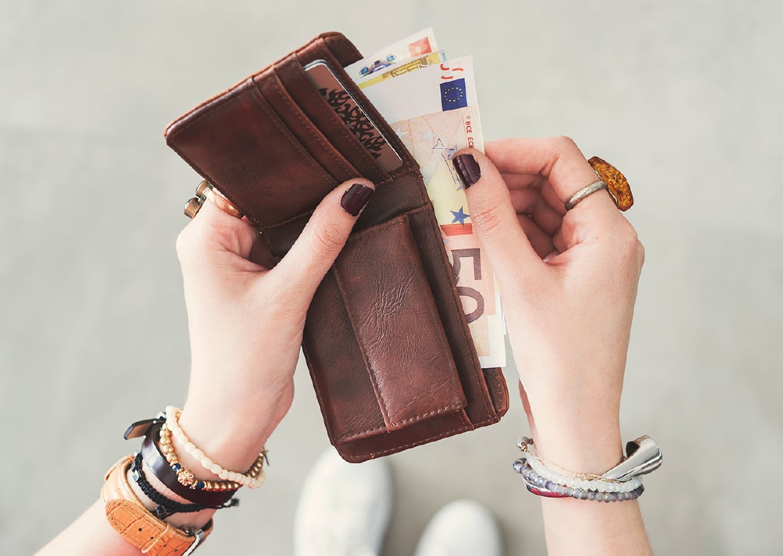 Imagem de uma mão segurando um porta-moeda marrom com notas de euros visíveis, destacando a organização e estilo no armazenamento do dinheiro.