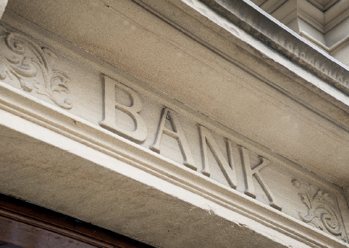 Detalhe de uma fachada de banco com a inscrição 'BANK' em destaque, evidenciando a arquitetura e design clássicos. Ideal para temas relacionados a finanças.