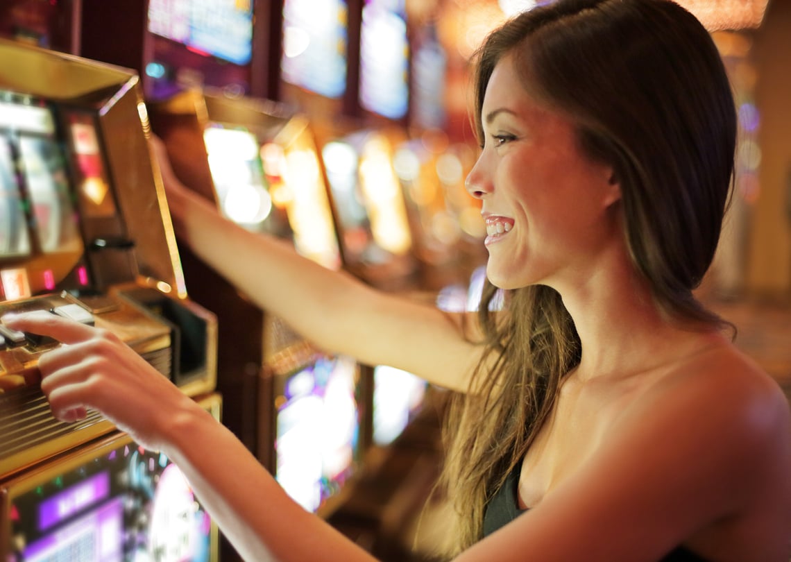 Mulher sorrindo enquanto joga em uma máquina caça-níqueis em um cassino, representando a emoção e a diversão das apostas.