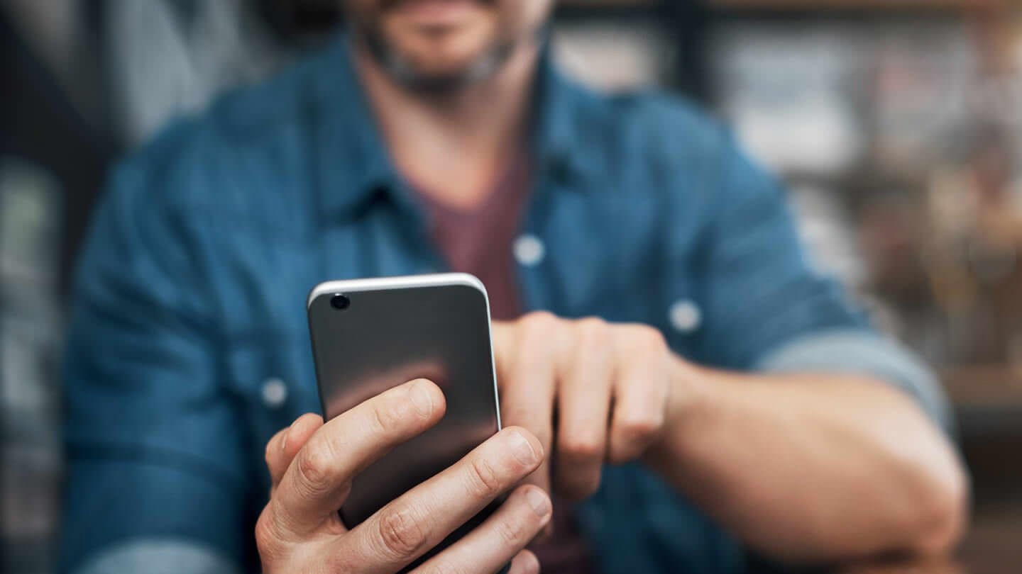 Homem usando smartphone em ambiente descontraído, destacando a popularidade da tecnologia móvel e a comunicação moderna.