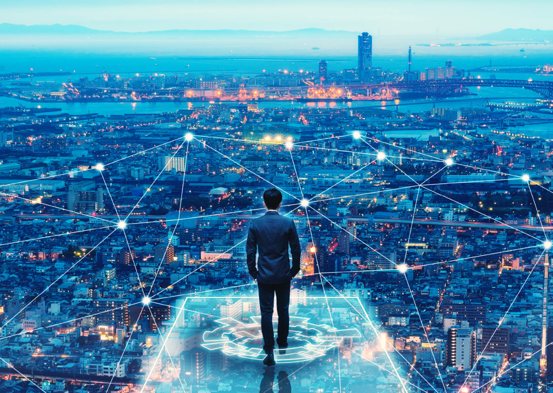 Homem de terno observando uma cidade iluminada à noite com uma rede de conexão digital ao redor, simbolizando a tecnologia e inovação na era digital.