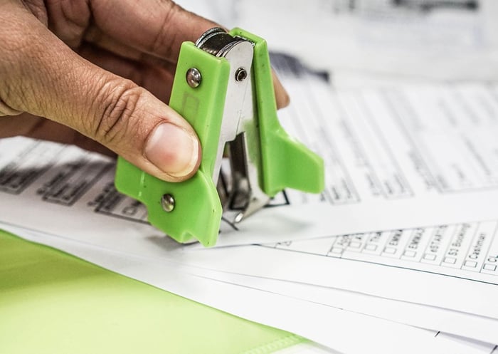 Pessoa utilizando uma emendadeira para fazer ajustes em documentos impressos, destaque para a ferramenta de cor verde posicionada sobre o papel.