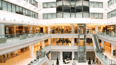 Interior de shopping moderno com varejo e clientes, onde soluções Glory de automação de processos, gestão de numerário e self‑checkout melhoram a experiência.