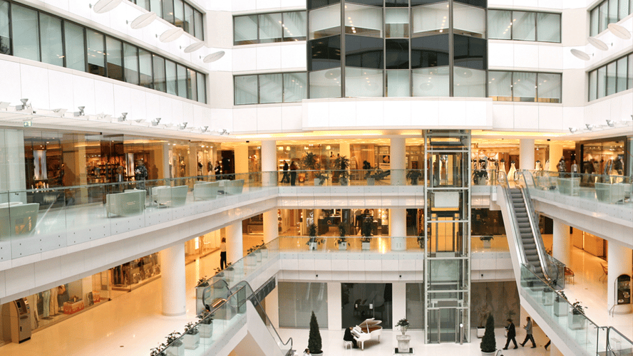 Interior de shopping moderno com varejo e clientes, onde soluções Glory de automação de processos, gestão de numerário e self‑checkout melhoram a experiência.