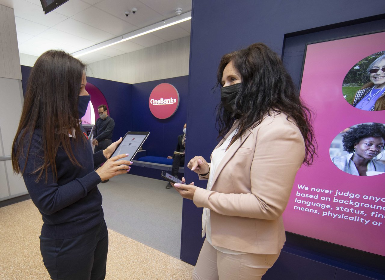 Imagem de duas mulheres conversando em um ambiente profissional, utilizando dispositivos móveis, com foco em inclusão e diversidade.
